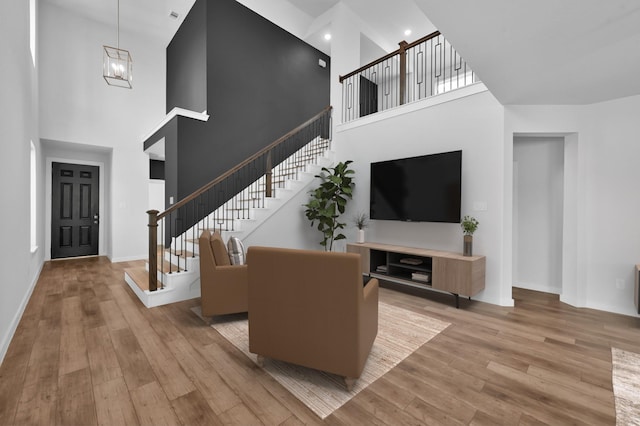 living area with a high ceiling, baseboards, a chandelier, light wood-style flooring, and stairs