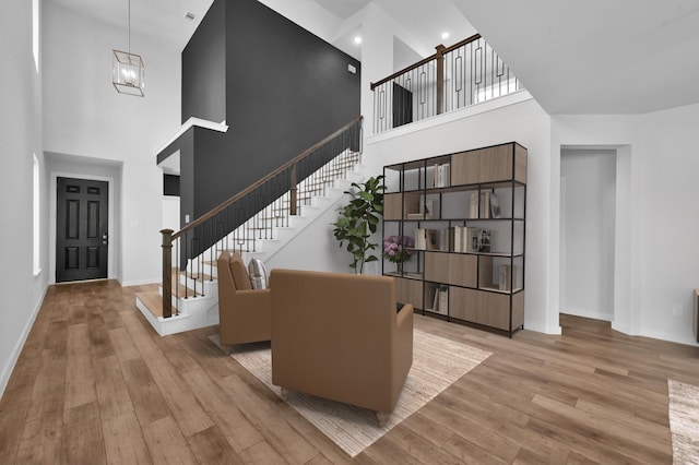 foyer with stairway, a towering ceiling, an inviting chandelier, baseboards, and light wood-style flooring