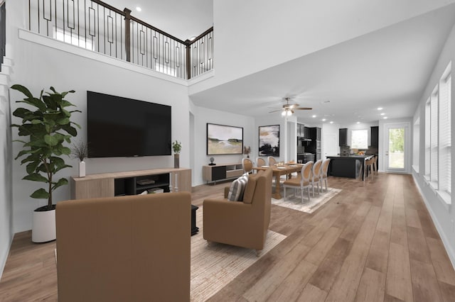living area featuring recessed lighting, a ceiling fan, a towering ceiling, and light wood-type flooring
