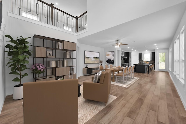 living area with recessed lighting, light wood-type flooring, a towering ceiling, and ceiling fan