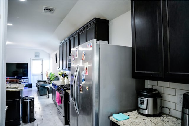 kitchen with dark cabinets, visible vents, vaulted ceiling, stainless steel appliances, and backsplash