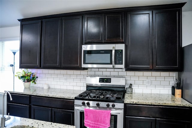 kitchen with dark cabinetry, appliances with stainless steel finishes, decorative backsplash, and light stone counters