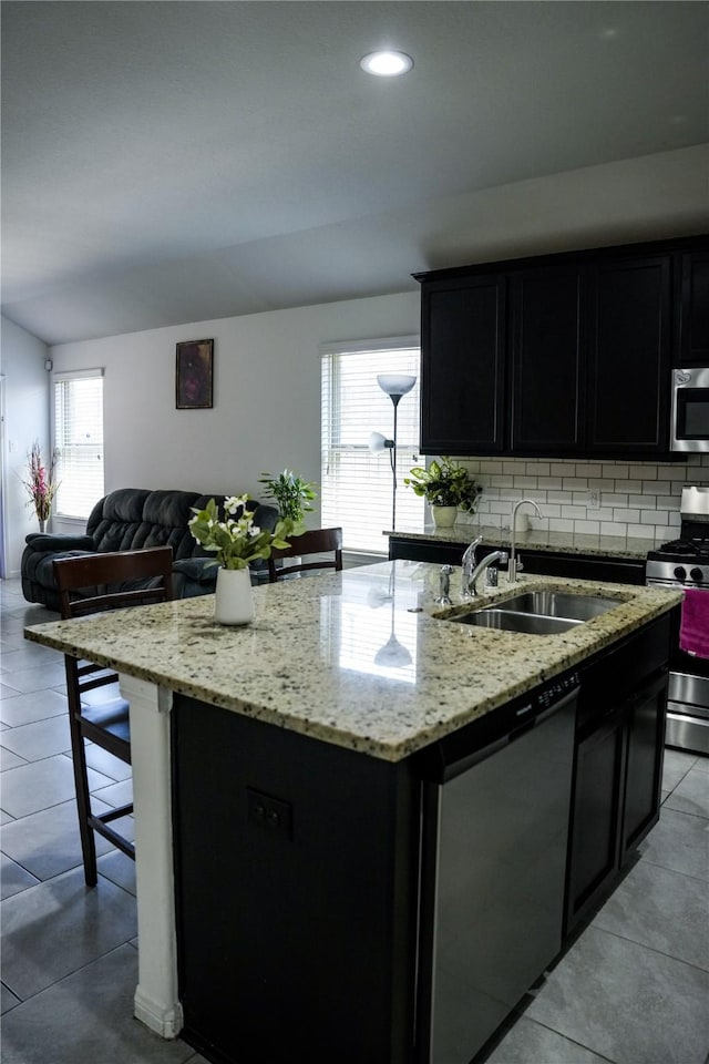 kitchen featuring appliances with stainless steel finishes, a kitchen island with sink, a sink, open floor plan, and backsplash