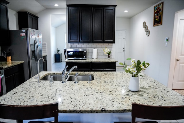 kitchen with a breakfast bar, light stone counters, backsplash, stainless steel appliances, and a sink