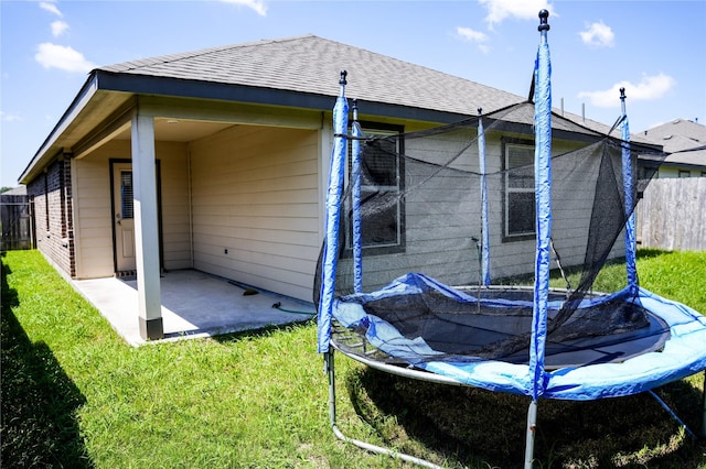 rear view of house featuring a trampoline, a patio area, fence, and a lawn