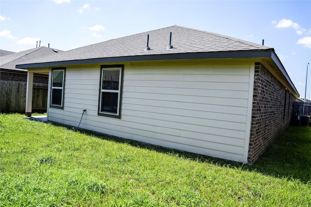 view of home's exterior with roof with shingles, brick siding, fence, and a lawn