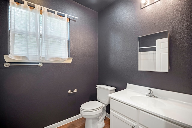 bathroom featuring vanity, toilet, wood finished floors, a textured wall, and baseboards