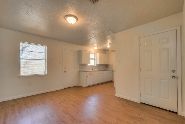 kitchen featuring baseboards, light countertops, white cabinetry, light wood finished floors, and a sink