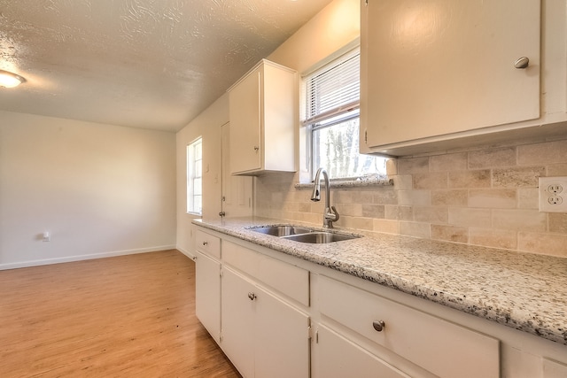 kitchen with light wood-style floors, white cabinetry, a sink, baseboards, and backsplash
