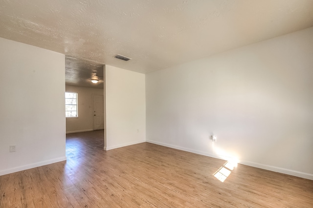 empty room featuring a textured ceiling, wood finished floors, baseboards, and visible vents