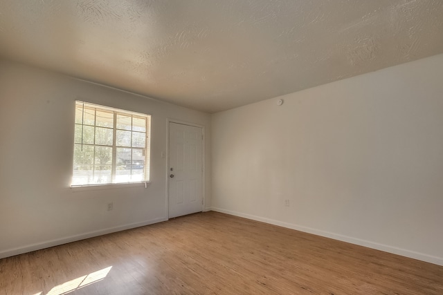 spare room featuring light wood-style floors, baseboards, and a textured ceiling
