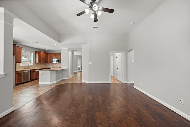 unfurnished living room featuring baseboards, visible vents, ceiling fan, a sink, and wood finished floors