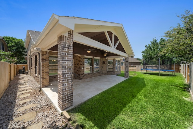 rear view of property with a trampoline, a patio area, a fenced backyard, ceiling fan, and a yard