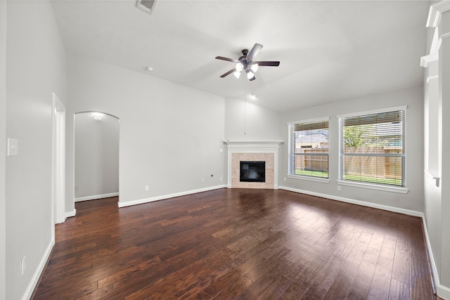 unfurnished living room with visible vents, arched walkways, a ceiling fan, dark wood finished floors, and a glass covered fireplace