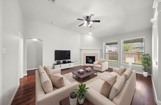 living room with baseboards, arched walkways, a ceiling fan, wood finished floors, and a glass covered fireplace