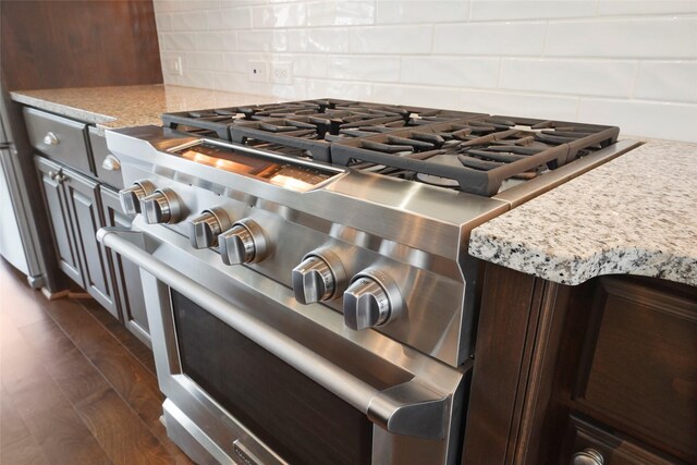 room details featuring dark brown cabinetry, high end range, light stone counters, and backsplash