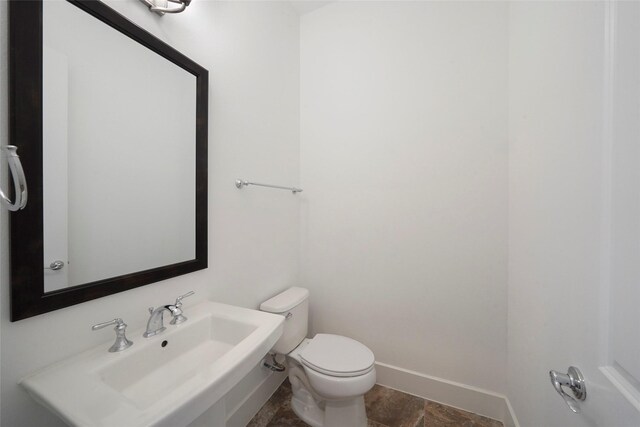 half bathroom with toilet, baseboards, and a sink