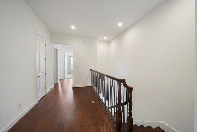 corridor featuring dark wood finished floors, baseboards, an upstairs landing, and recessed lighting
