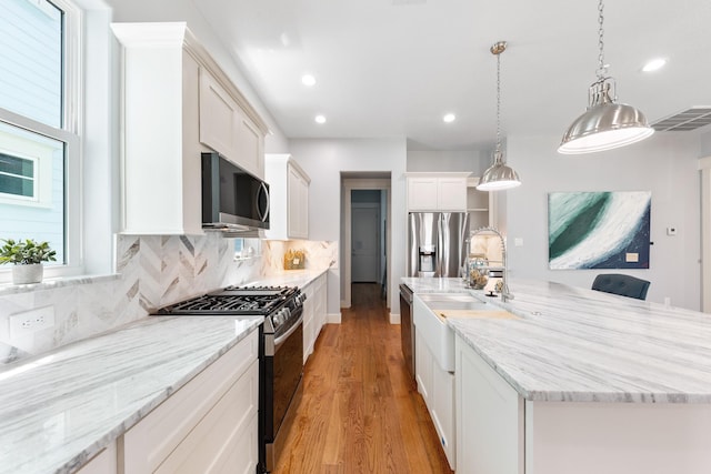 13 Caravelle Ct, Galveston, TX 77554 - kitchen with appliances with stainless steel finishes, light wood finished floors, a large island, white cabinets, and decorative backsplash