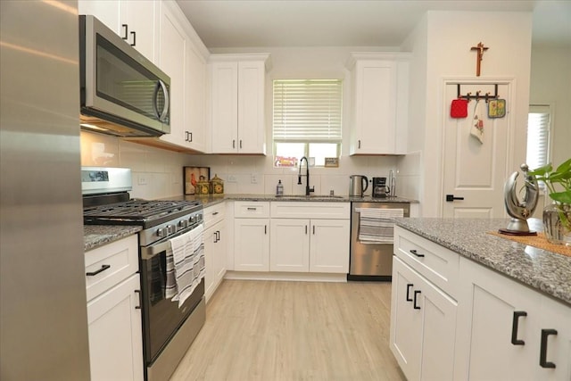 17014 Wild Stream Ct, Conroe, TX 77302 - kitchen featuring a sink, decorative backsplash, stainless steel appliances, light wood-type flooring, and white cabinets