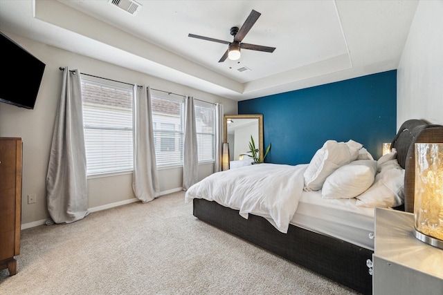 carpeted bedroom featuring ceiling fan, a tray ceiling, visible vents, and baseboards