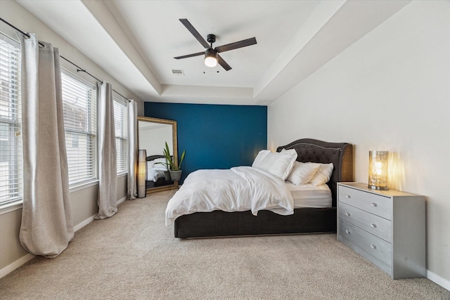 bedroom featuring visible vents, baseboards, light colored carpet, a tray ceiling, and a ceiling fan