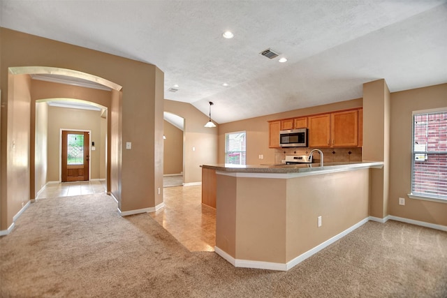 kitchen with a peninsula, light colored carpet, arched walkways, vaulted ceiling, and stainless steel appliances