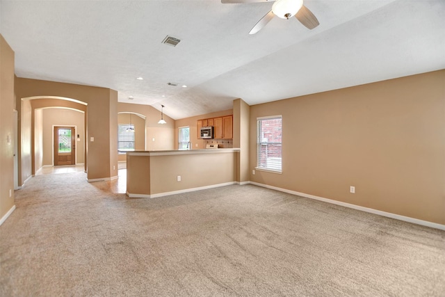 unfurnished living room with ceiling fan, visible vents, arched walkways, lofted ceiling, and light carpet