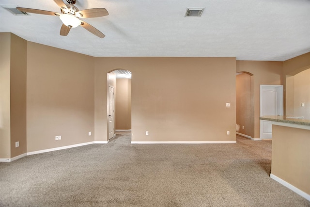 unfurnished room with ceiling fan, visible vents, arched walkways, baseboards, and light carpet