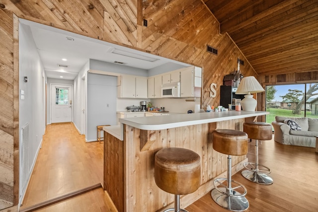 kitchen with white microwave, light countertops, wood walls, light wood-style floors, and visible vents