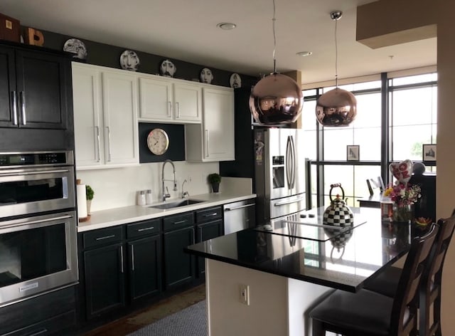 kitchen with a breakfast bar area, hanging light fixtures, a sink, dark cabinetry, and stainless steel appliances