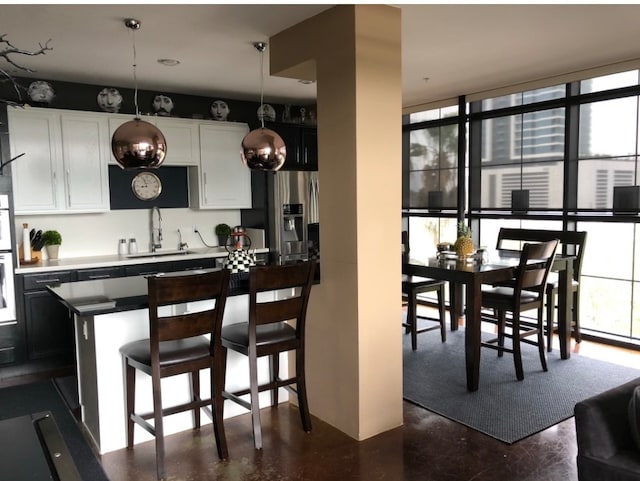 kitchen featuring a sink, stainless steel fridge with ice dispenser, concrete floors, a breakfast bar, and white cabinetry