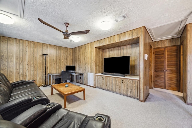 living room featuring wooden walls, visible vents, ceiling fan, and light colored carpet