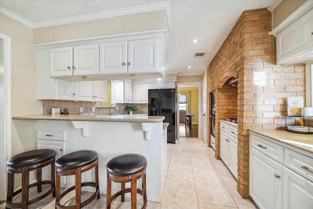 kitchen with black fridge, a breakfast bar, a peninsula, backsplash, and white cabinetry