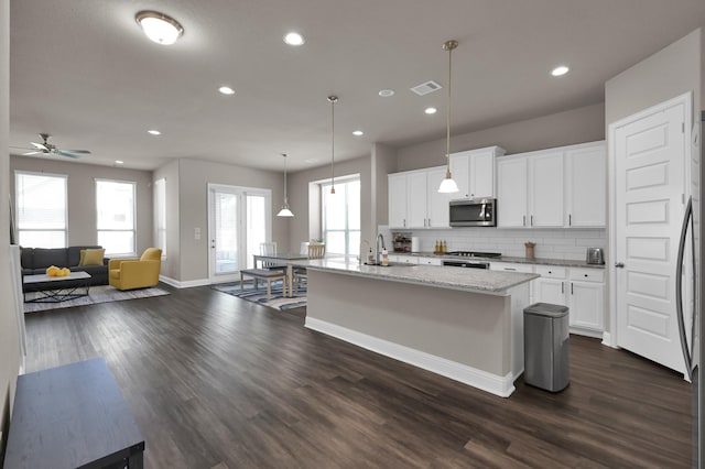 17052 Easter Lily Dr, Conroe, TX 77385 - kitchen featuring stainless steel microwave, decorative backsplash, dark wood finished floors, a kitchen island with sink, and light stone counters