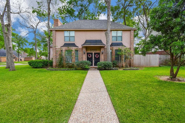 tudor home featuring a chimney, a front yard, brick siding, a standing seam roof, and fence