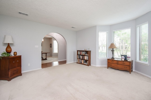 sitting room with arched walkways, carpet, visible vents, and a textured ceiling