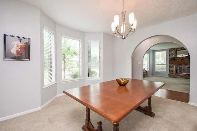 dining room featuring a fireplace, arched walkways, a textured ceiling, a notable chandelier, and baseboards