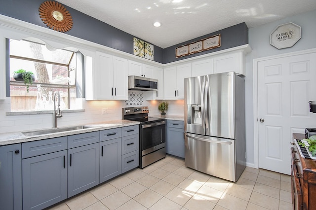kitchen featuring white cabinets, a sink, light tile patterned flooring, and appliances with stainless steel finishes