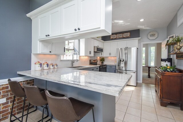 kitchen with white cabinets, appliances with stainless steel finishes, a peninsula, light tile patterned flooring, and light stone counters