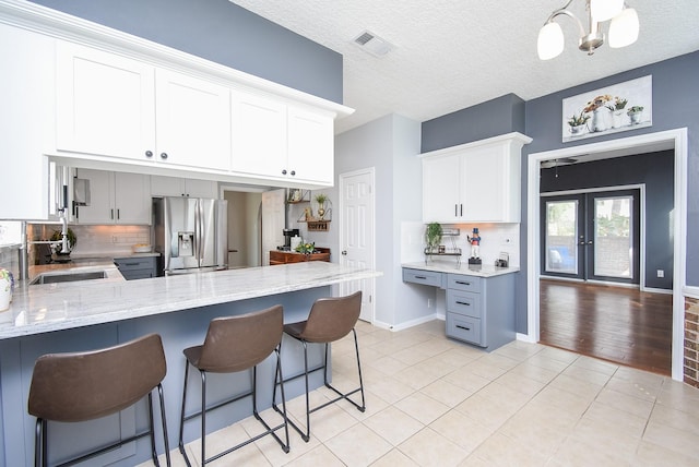 kitchen featuring light tile patterned flooring, stainless steel refrigerator with ice dispenser, light stone countertops, visible vents, and decorative backsplash