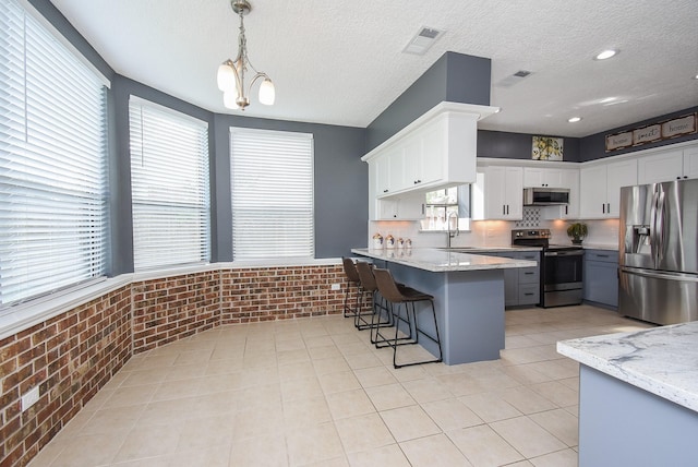 kitchen with brick wall, a sink, appliances with stainless steel finishes, a kitchen breakfast bar, and a peninsula
