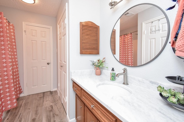 full bathroom featuring vanity, a textured ceiling, visible vents, and wood finished floors