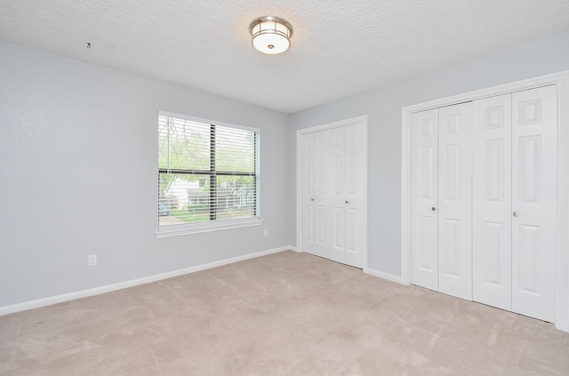 unfurnished bedroom with baseboards, carpet flooring, two closets, and a textured ceiling