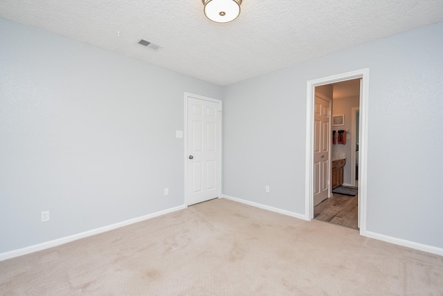 spare room featuring visible vents, baseboards, light colored carpet, and a textured ceiling