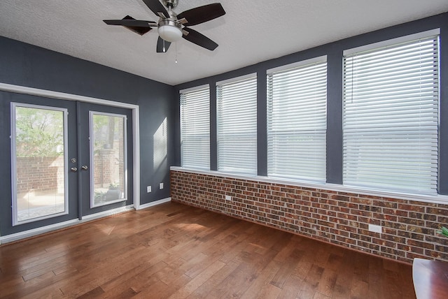 spare room with brick wall, hardwood / wood-style flooring, a ceiling fan, and a textured ceiling
