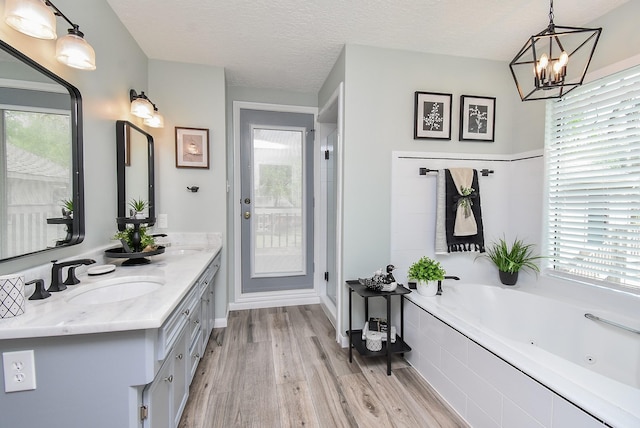 full bath with a sink, a jetted tub, wood finished floors, and a textured ceiling