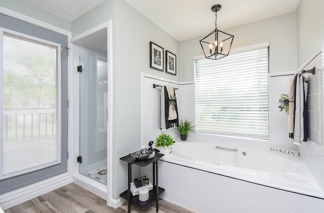 full bathroom featuring a notable chandelier, a textured ceiling, a shower stall, wood finished floors, and a garden tub