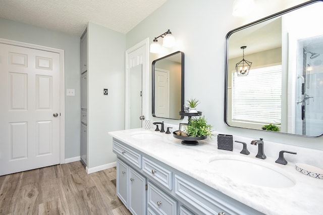 bathroom with a textured ceiling, wood finished floors, double vanity, and a sink