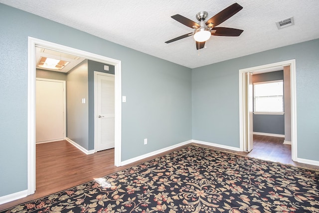 unfurnished bedroom with a textured ceiling, a ceiling fan, visible vents, wood finished floors, and baseboards